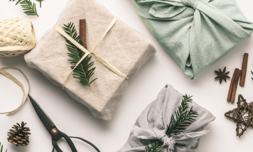 Sustainable holiday gifts wrapped in fabric with natural decorations like pine sprigs, cinnamon sticks, and twine, surrounded by eco-friendly wrapping materials.