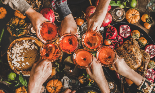  A festive Friendsgiving table filled with seasonal foods, colorful fruits, and friends toasting with glasses, creating a warm, celebratory atmosphere.