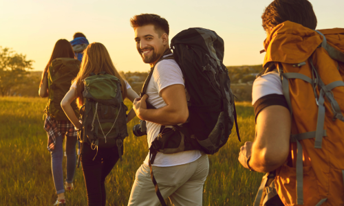 A group of friends hiking through a field at sunset, with one person smiling back at the camera