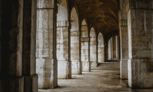 Ancient stone arcade with a series of arches casting shadows on the floor, conveying a sense of historical architecture.