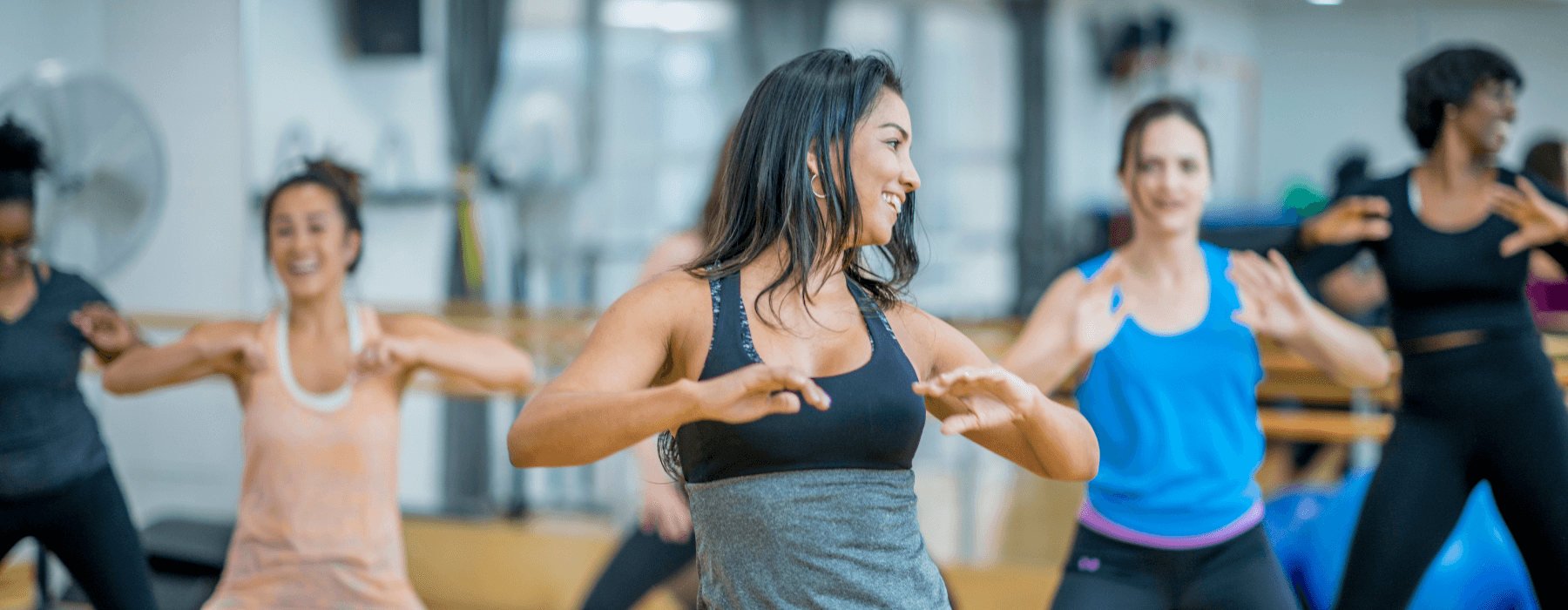 A group of people participating in a dance fitness class, smiling and performing coordinated movements.