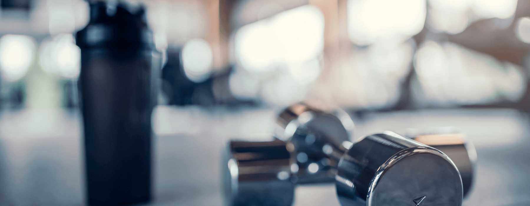 Two dumbbells and a black water bottle sitting on the floor of a gym.